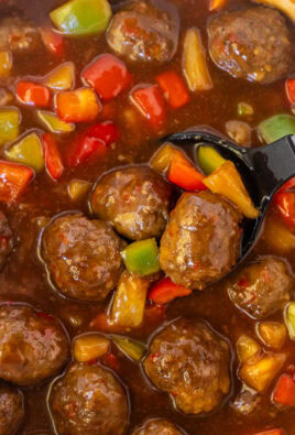 Crock pot of sweet and sour meatballs with a spoon.