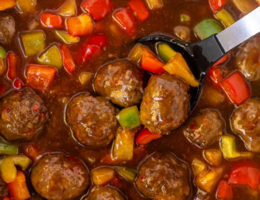 Crock pot of sweet and sour meatballs with a spoon.