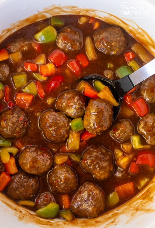 Crock pot of sweet and sour meatballs with a spoon.