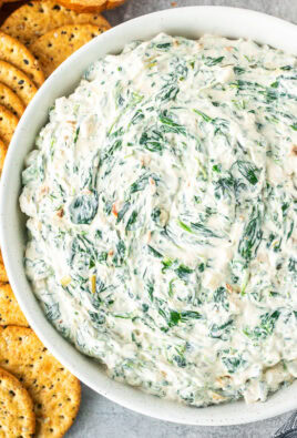 Large bowl of spinach dip next to crackers and sliced bread.