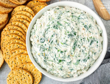 Large bowl of spinach dip next to crackers and sliced bread.