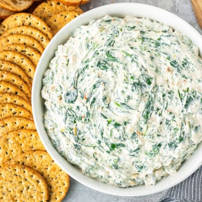 Large bowl of spinach dip next to crackers and sliced bread.