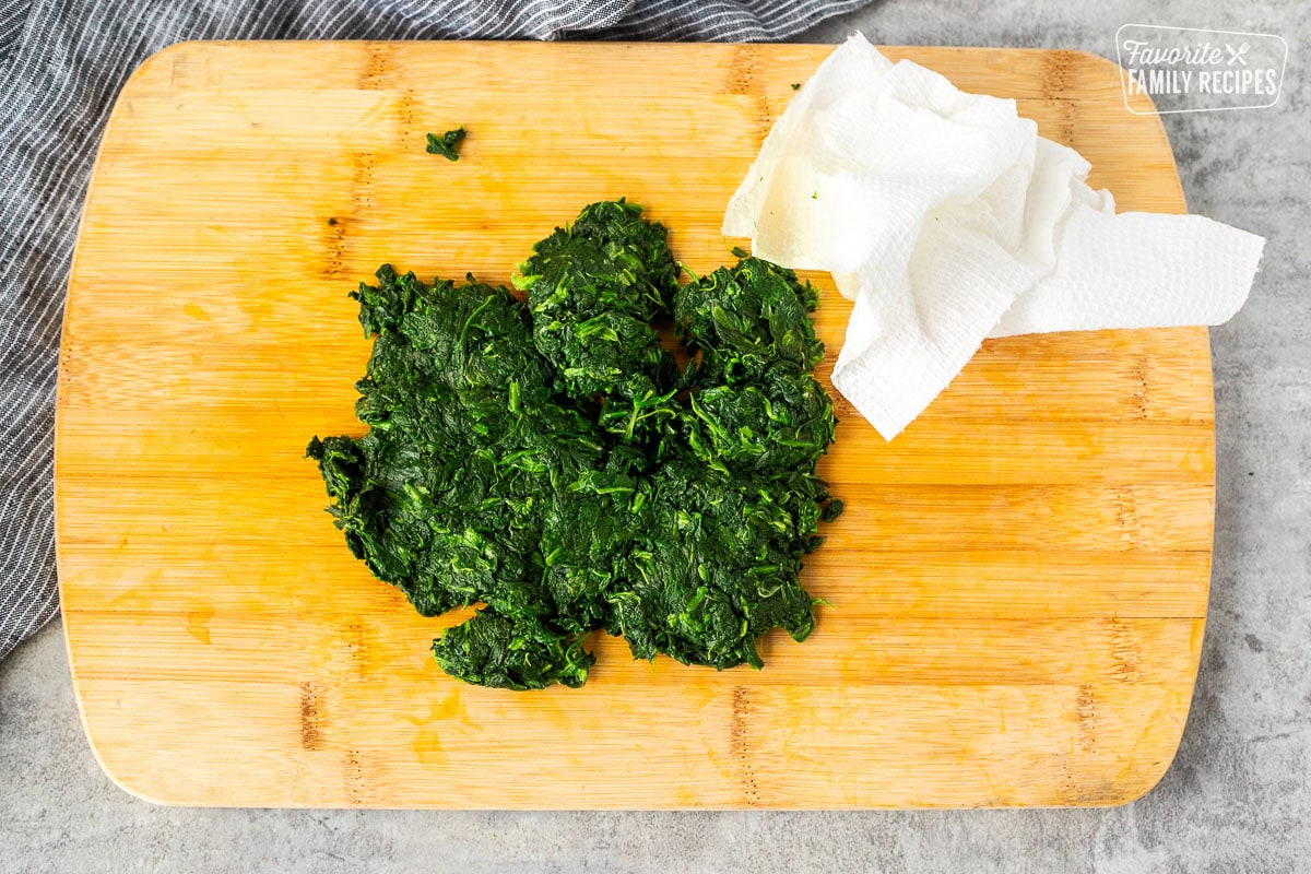 Cutting board with squeezed out spinach and a paper towel.