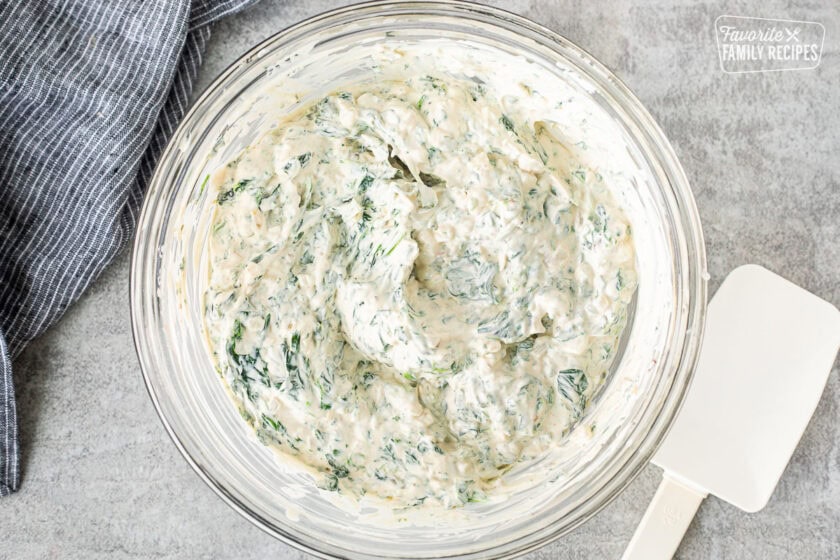 Glass mixing bowl with combined spinach dip. Spatula on the side.