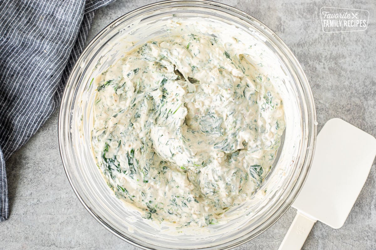 Glass mixing bowl with combined spinach dip. Spatula on the side.