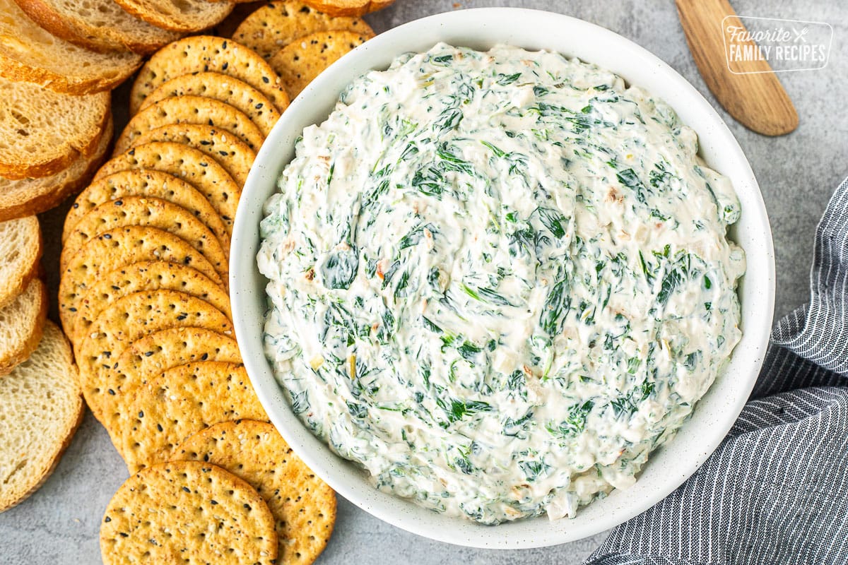 Large bowl of spinach dip next to crackers and sliced bread.