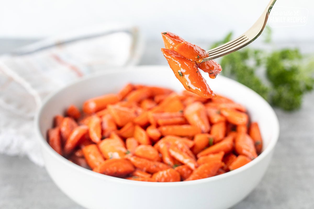 Candied carrots with a fork over a large bowl of carrots.