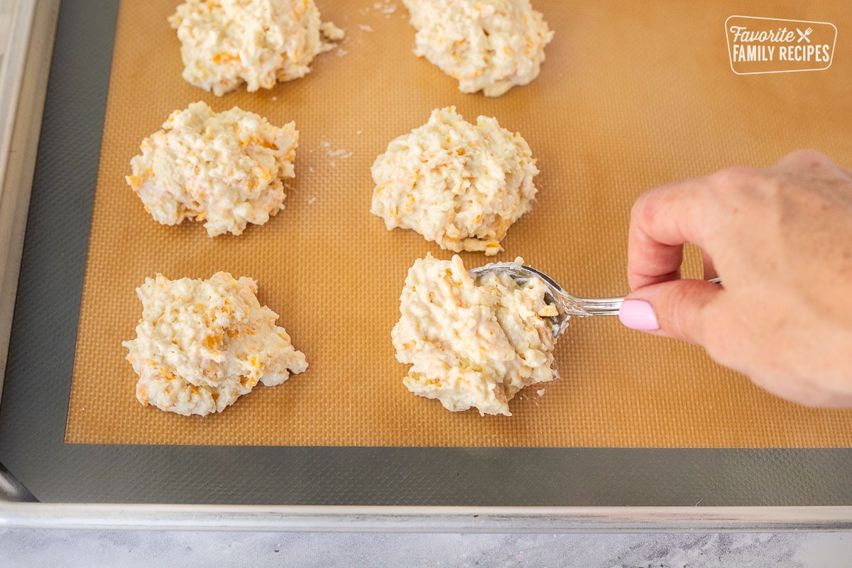 Placing Red Lobster Cheddar Bay Biscuits onto a baking sheet with a spoon.