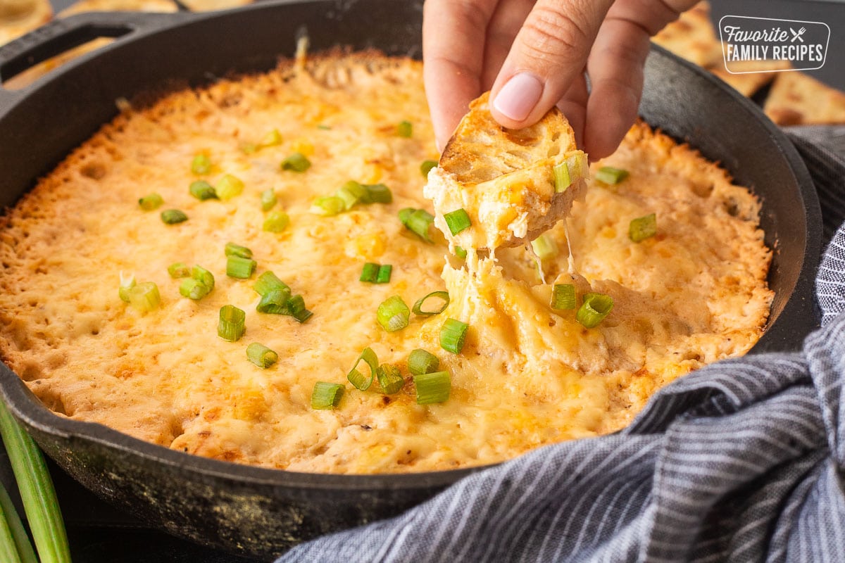 Dipping a slice of bread into a skillet of Hot Crab Dip.