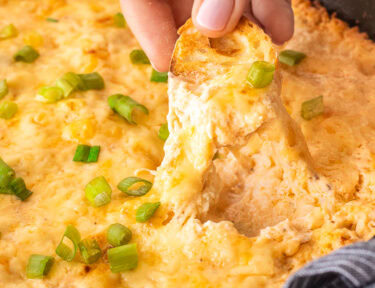 Dipping a slice of bread into a skillet of Hot Crab Dip.