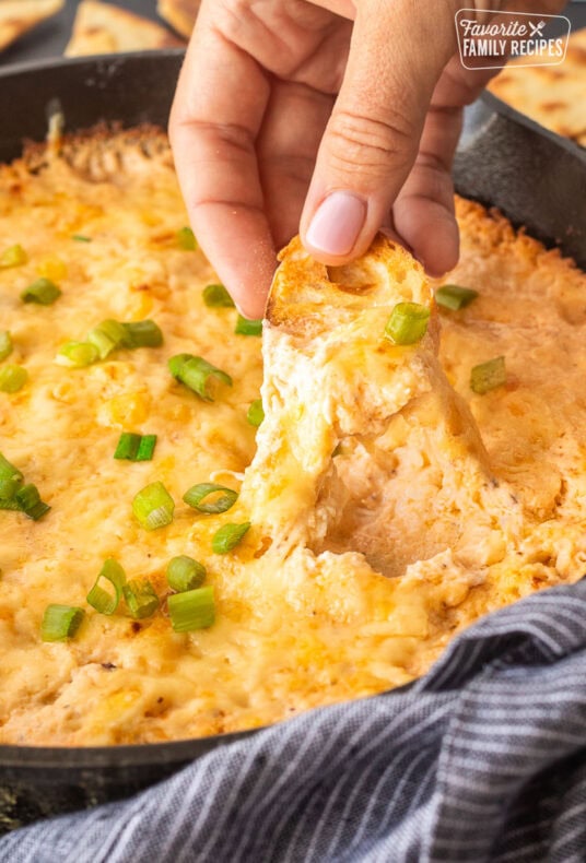 Dipping a slice of bread into a skillet of Hot Crab Dip.