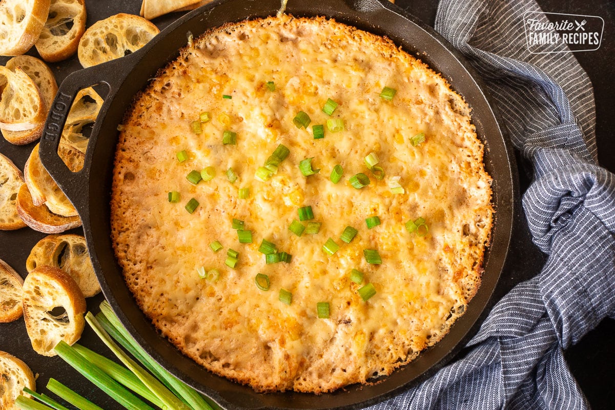 Baked Hot Crab dip in a skillet with green onion on top. Bread slices on the side.