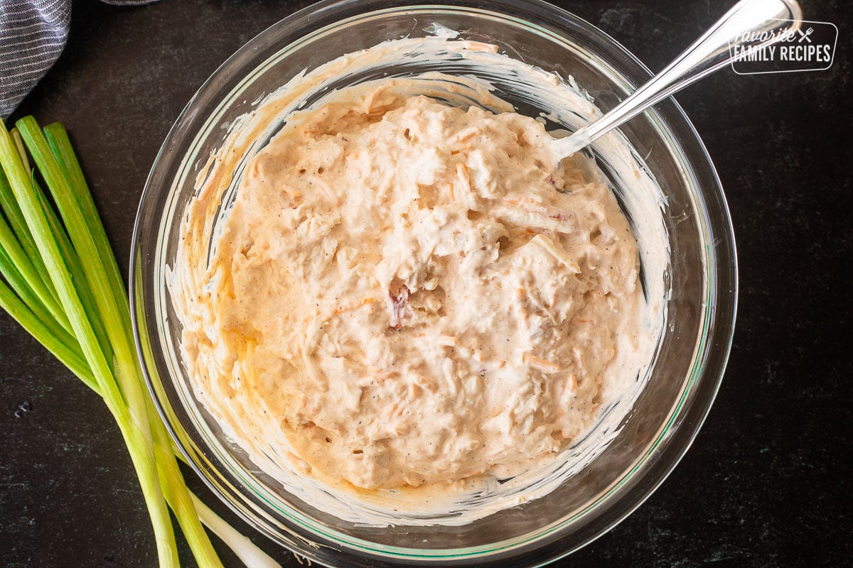 Glass bowl with Hot Crab Dip mixing with spoon.