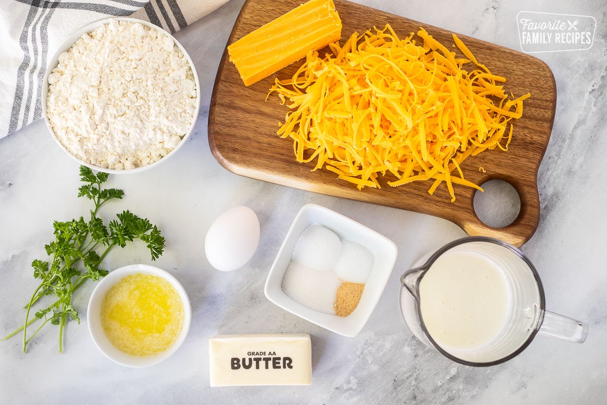 Ingredients to make Cheddar Bay Biscuits including shredded cheddar cheese, flour, egg, spices, buttermilk, frozen butter, melted butter and parsley.