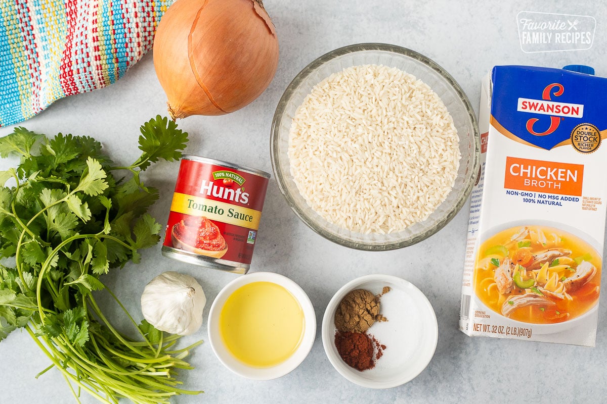 Ingredients to make instant pot Mexican rice including rice, chicken broth, spices, oil, tomato sauce, cilantro, onion, and garlic.