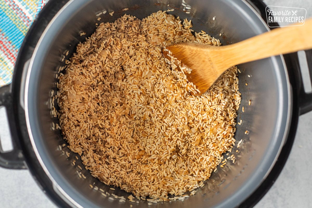 Instant pot pot with brown brown rice and onions and garlic with wooden spoon.