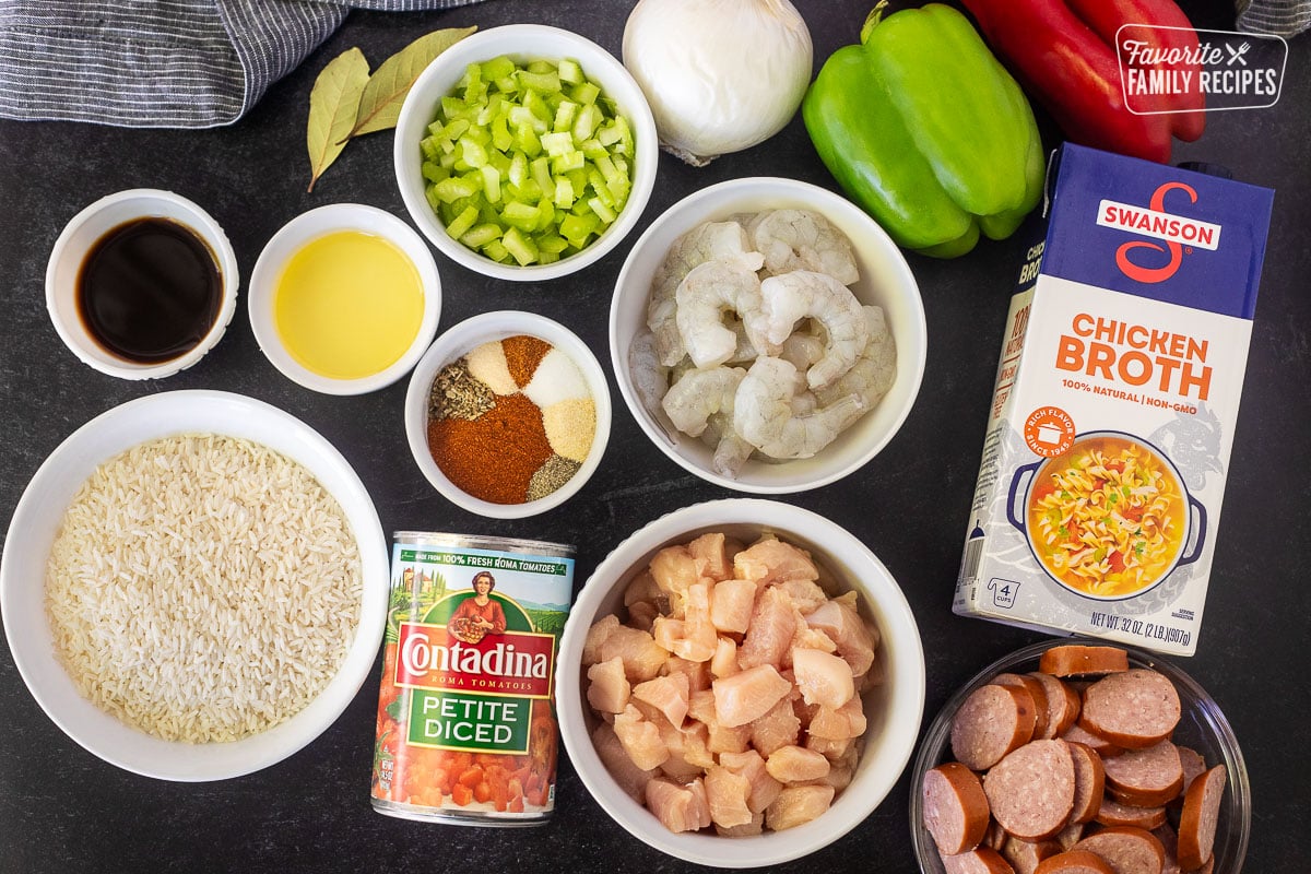 Ingredients to make jambalaya including green bell pepper, red bell pepper, onion, celery, oil, Worcester sauce, rice, petite diced tomatoes, spices, cut chicken, raw shrimp, kielbasa and chicken broth.