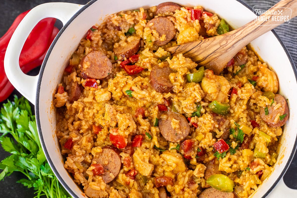 Dutch oven with Jambalaya garnished with fresh parsley and pepper. Wooden spoon resting inside.