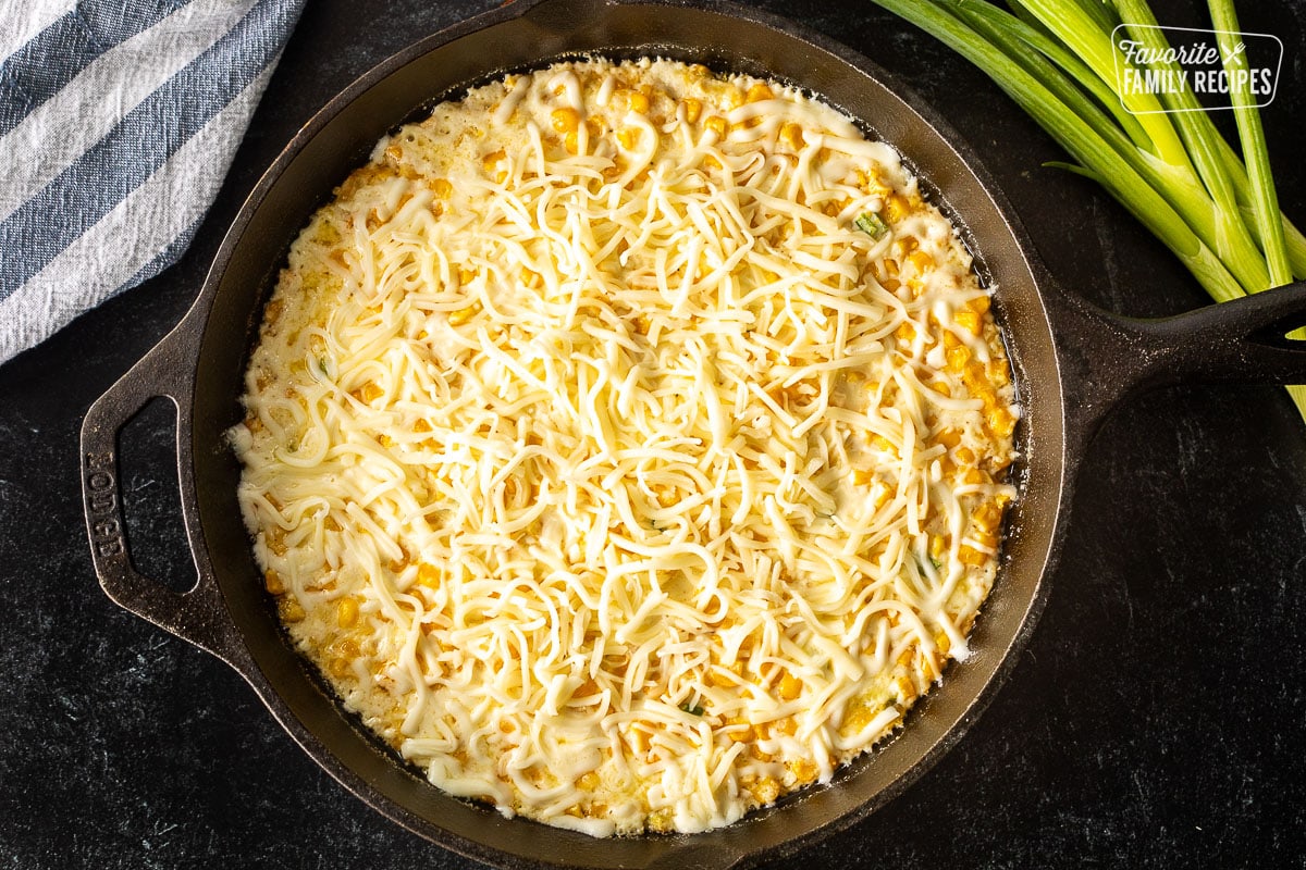 Skillet with hot corn cheese and shredded mozzarella cheese on top.