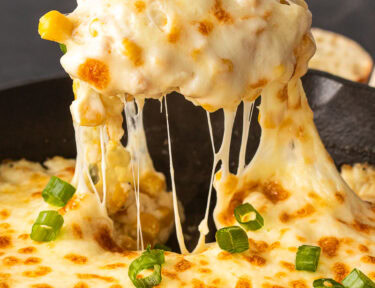 Spoon pulling out Corn Cheese scoop out of a skillet.