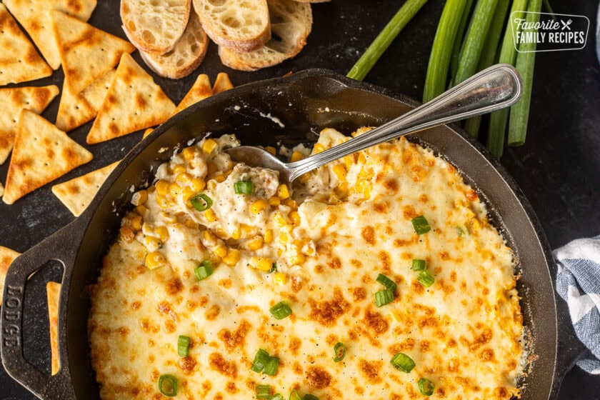 Corn cheese in a skillet with green onions and a spoon resting in the dish.