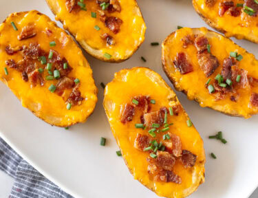 Loaded potato skins with melted cheese, bacon, and chives on a platter.