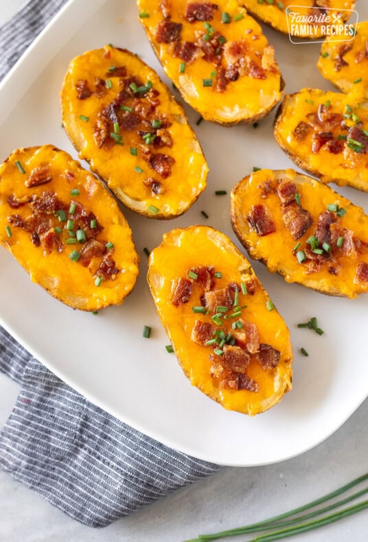 Loaded potato skins with melted cheese, bacon, and chives on a platter.