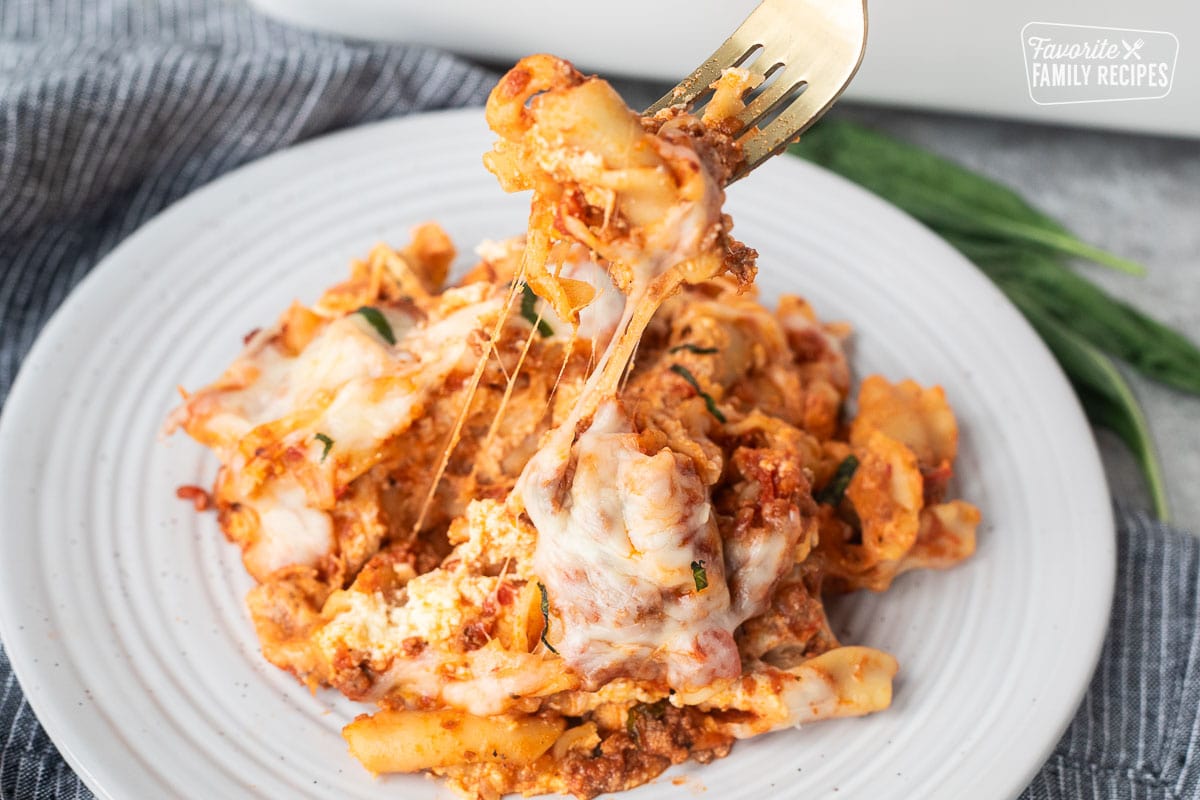 Fork lifting up a cheesy bite of lasagna casserole from a plate.