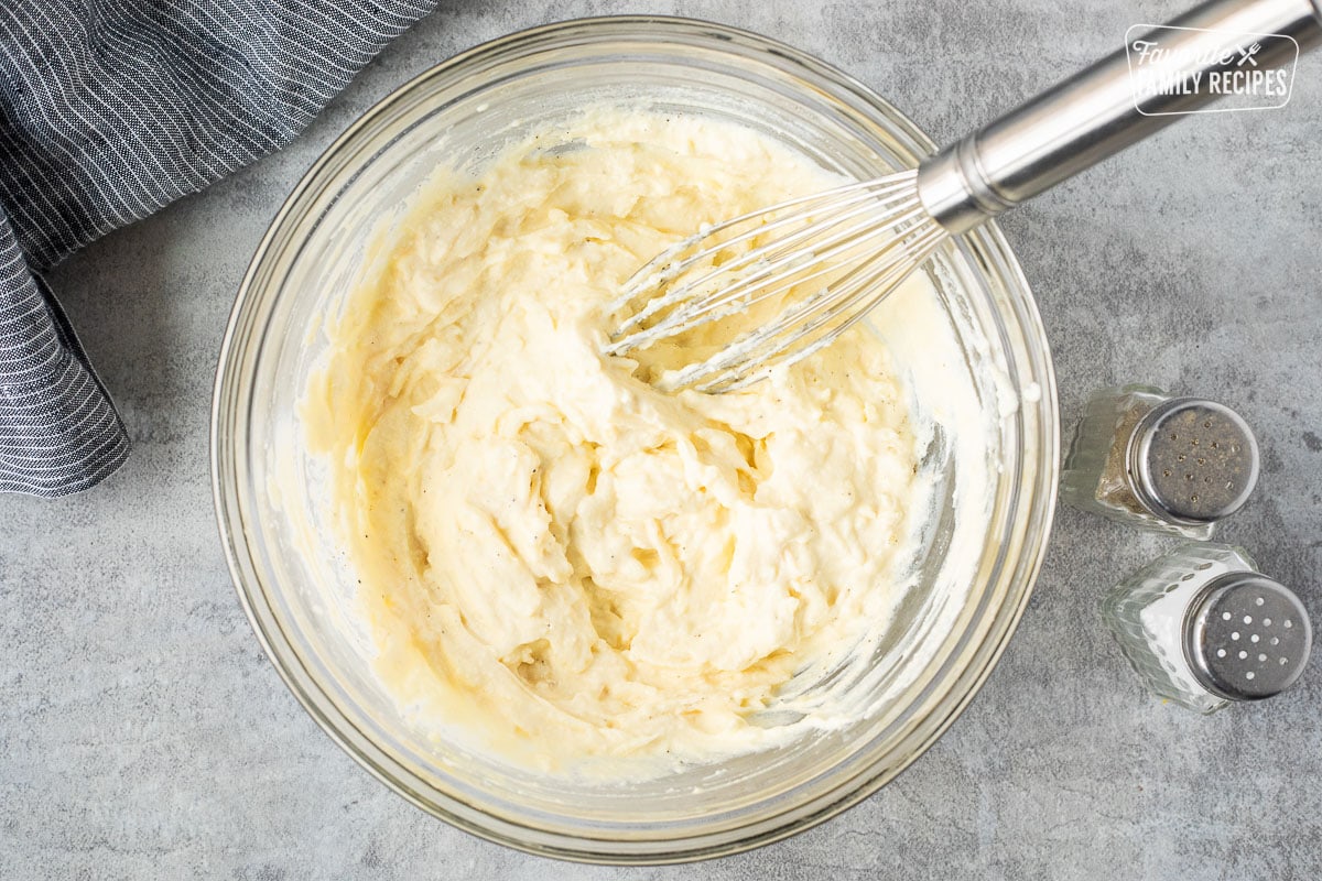 Glass mixing bowl with combined cheeses and whisk. Salt and pepper on the side.