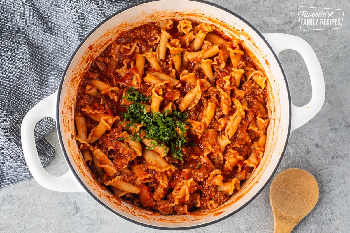 Dutch oven with sauce and noodles combined and fresh basil on top.