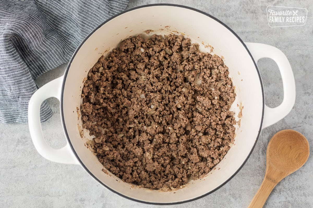 Dutch oven with cooked ground beef and onion. Wooden spoon on the side.