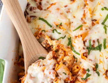 Wooden spoon scooped lasagna casserole resting in a baking dish.