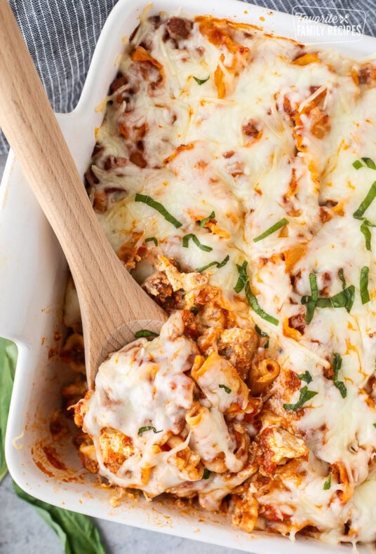 Wooden spoon scooped lasagna casserole resting in a baking dish.