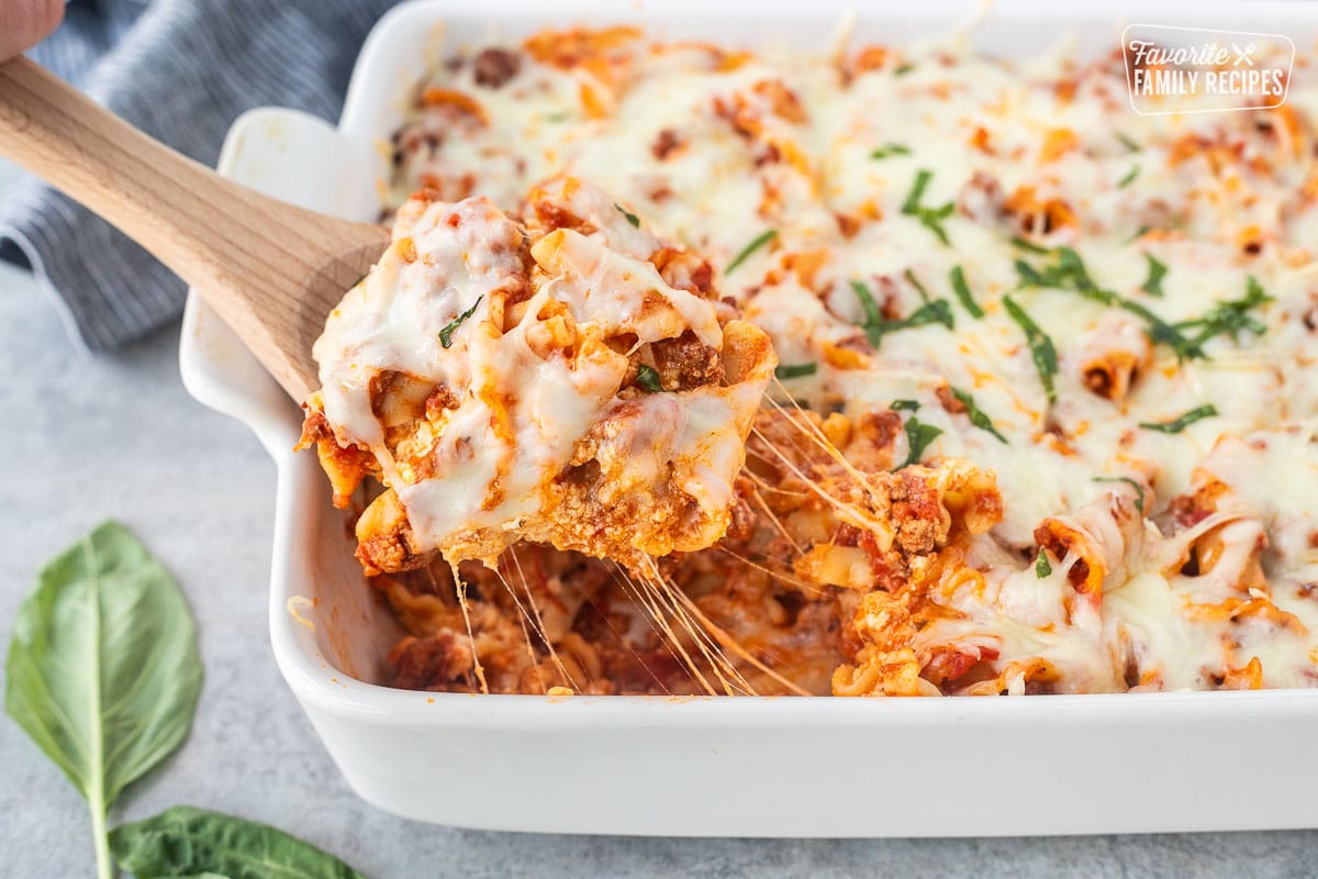 Wooden spoon lifting a serving of lasagna casserole as the cheese is pulling.