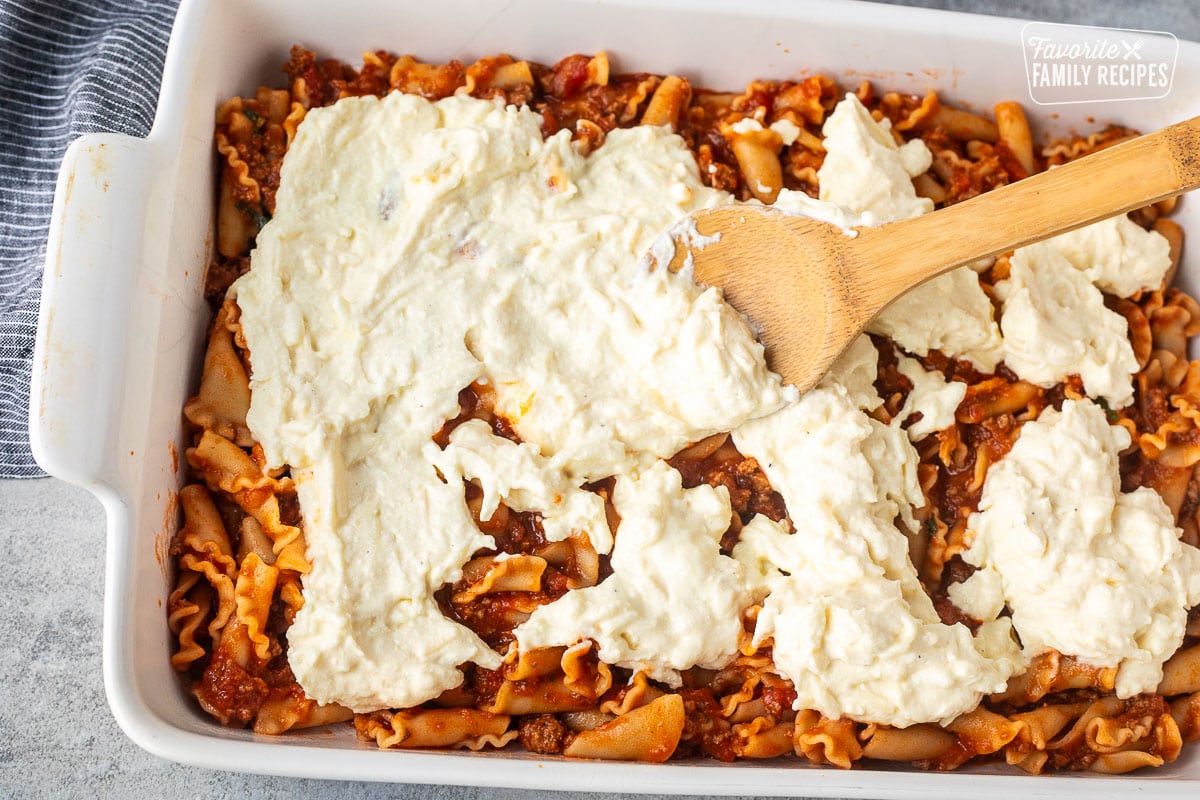 Baking dish with layer of marinara pasta and cheese layer spread on top with a wooden spoon.