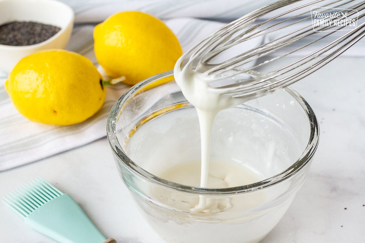 Whisk drizzling the glaze over a bowl for Lemon Poppy Seed Muffins.