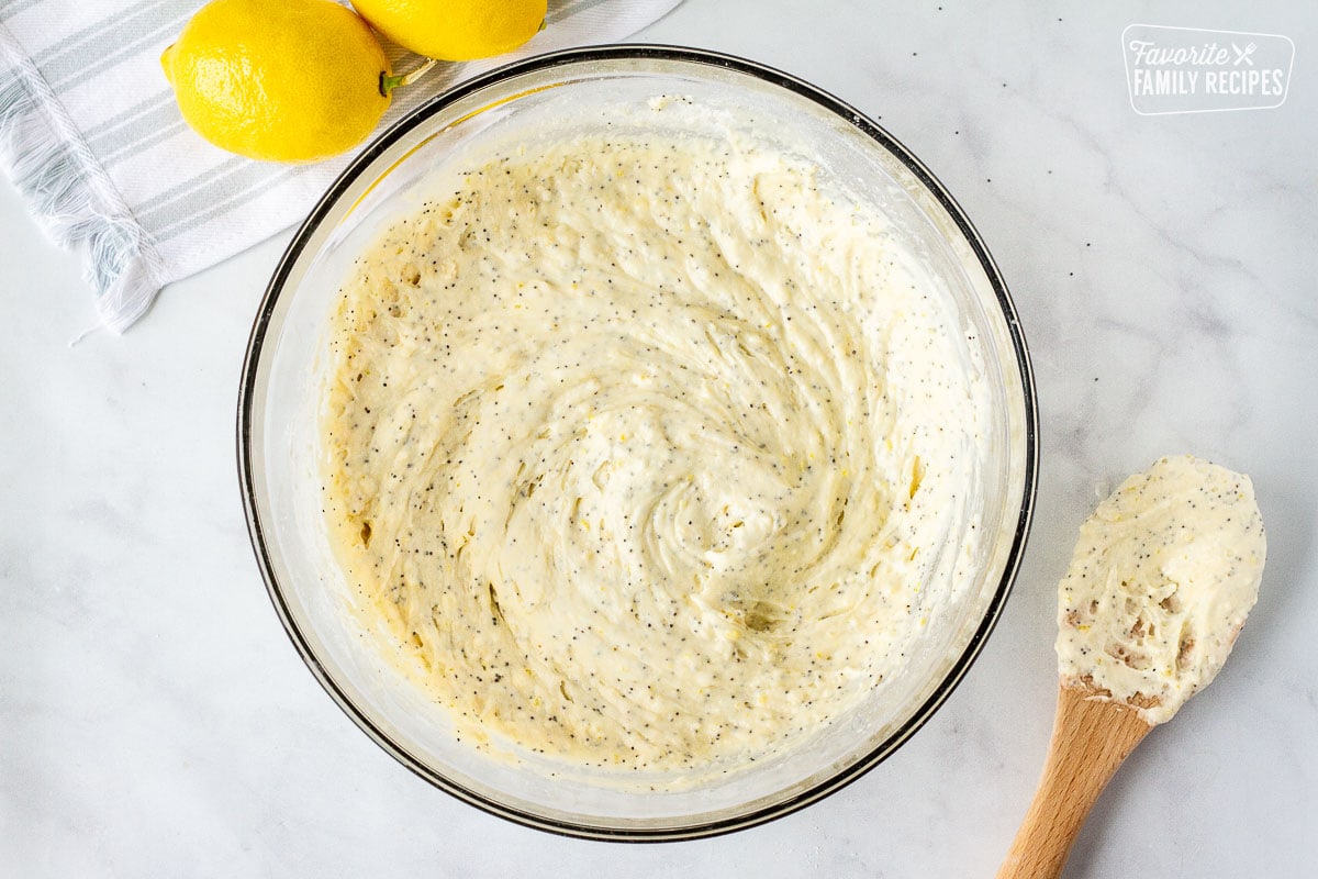 Lemon poppy seed muffin batter in a glass bowl. Wooden spoon on the side.