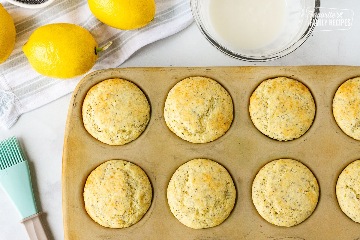 Baked Lemon Poppy Seed Muffins next to the bowl of glaze and a brush.