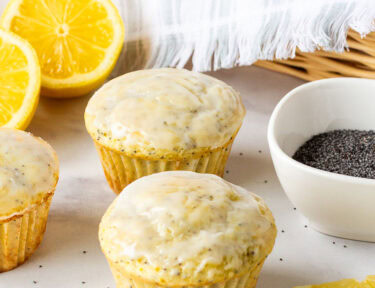 Three Lemon Poppy Seed Muffins in front of a basket of muffins.