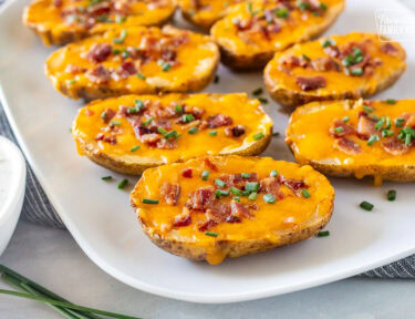 Side of loaded potato skins on a platter with melted cheddar cheese, crispy bacon, and chives.