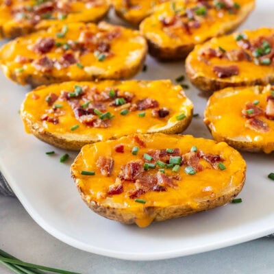 Side of loaded potato skins on a platter with melted cheddar cheese, crispy bacon, and chives.