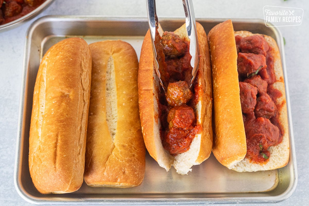 Placing meatballs into cut rolls with tongs.