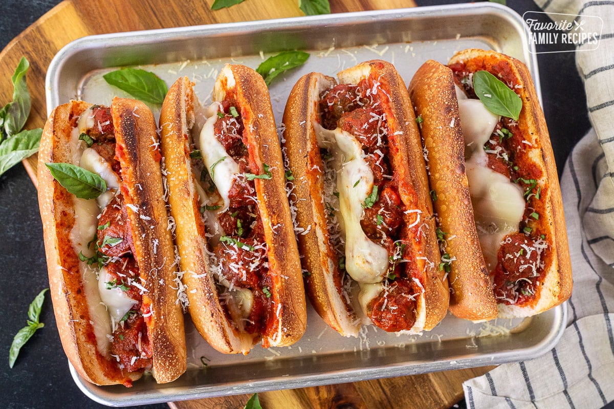 Baking sheet with four baked Meatball Sandwiches with fresh parmesan cheese grated on top and basil.