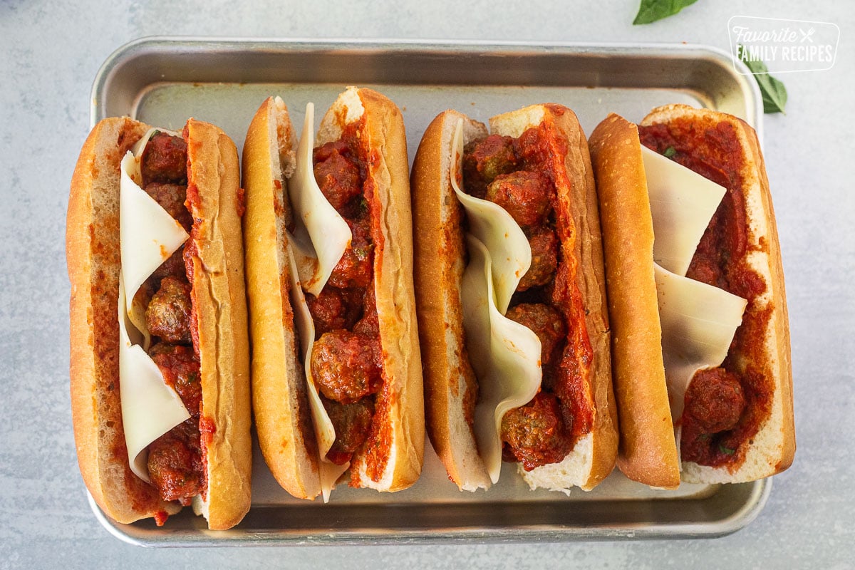 Four Meatball Sandwiches lined up on a baking sheet with unmelted cheese.