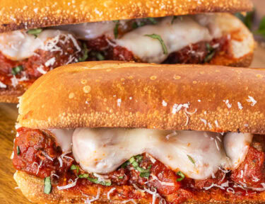 Three Meatball Sandwiches with melted cheese, fresh basil and grated parmesan on a toasted roll.