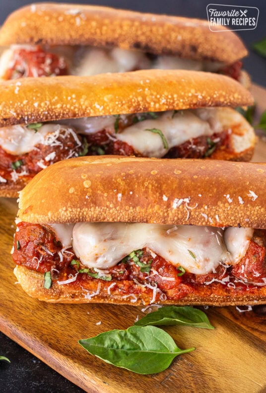 Three Meatball Sandwiches with melted cheese, fresh basil and grated parmesan on a toasted roll.