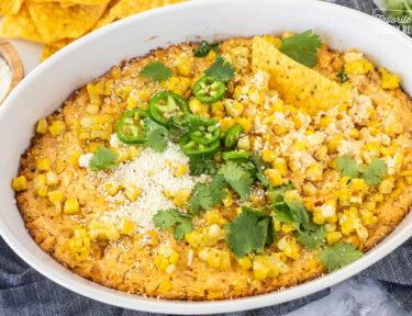 Baked Mexican Street Corn Dip in a dish toped with jalapeño, cilantro and cojita cheese with tortilla chips.