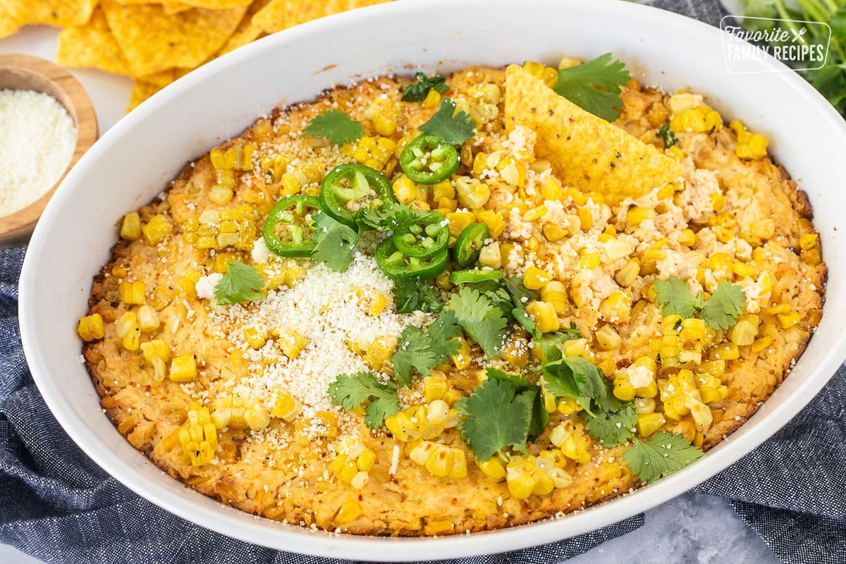 Baked Mexican Street Corn Dip in a dish toped with jalapeño, cilantro and cojita cheese with tortilla chips.