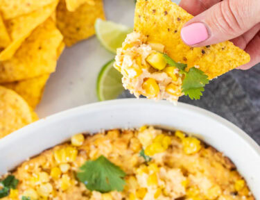 Hand holding a chip with Mexican Street Corn Dip in a dish.