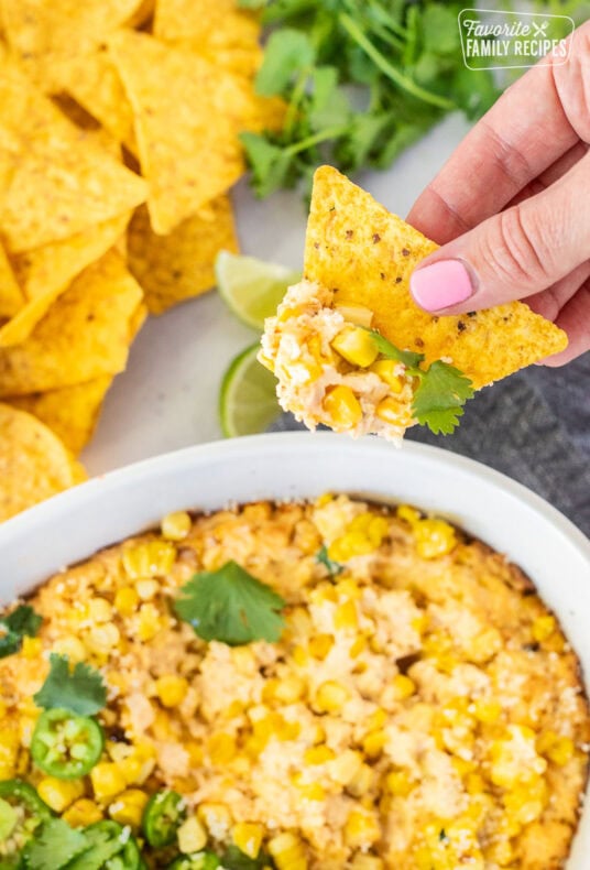 Hand holding a chip with Mexican Street Corn Dip in a dish.